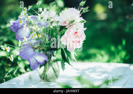 Bouquet von weißen Pfingstrosen, Kamillen und Iris Blumen in Glasvase. Sommer Hintergrund. Getönte Foto Stockfoto