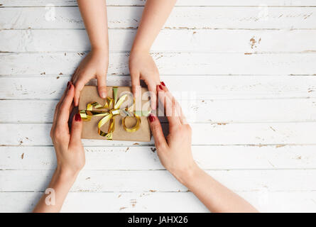 Frau mit ihrem Kind ein Geschenk in der Hand auf weißem Holz Hintergrund halten. Stockfoto