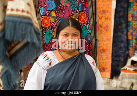 OTAVALO, ECUADOR - 17. Mai 2017: Nahaufnahme von eine nicht identifizierte hispanische indigene Frau tragen traditionelle Kleidung der Anden und Halskette, posiert für die Kamera im bunten Stoffen Hintergrund Stockfoto