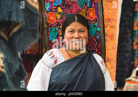 OTAVALO, ECUADOR - 17. Mai 2017: Nahaufnahme von eine nicht identifizierte hispanische indigene Frau tragen traditionelle Kleidung der Anden und Halskette, posiert für die Kamera im bunten Stoffen Hintergrund Stockfoto