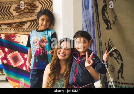 OTAVALO, ECUADOR - 17. Mai 2017: Schöne junge Frau umarmt, zwei schöne wenig indigene Mädchen in bunten Stoffen Hintergrund Stockfoto