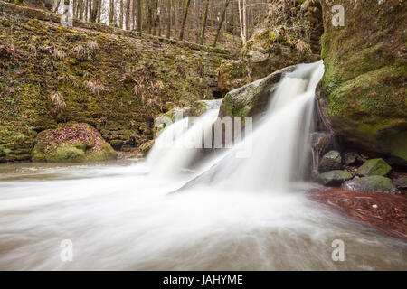 tief im Wald gibt es einen kleinen Wasserfall in der Schweiz in Luxemburg mit Schnee Stockfoto