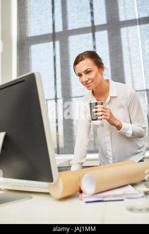 Junge Frau mit Kaffee an ihrem Schreibtisch mit Computer und internet Stockfoto