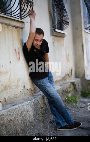 Mann und eine Stadt. Betrunkener Mann steht bereit, um an der Wand anlehnen. Stockfoto