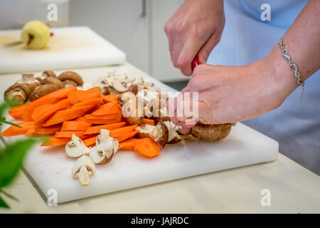 Weibliche Hände hacken Karotten und Pilze auf weiß geschnitten board Stockfoto