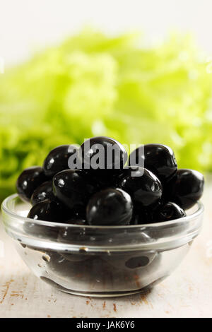 Schwarze Oliven in einer Schüssel transparent und Salat Stockfoto