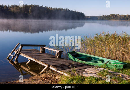 Alte hölzerne Angelboot/Fischerboot und alte Brücke auf dem nebligen See in Morgenstunde Stockfoto