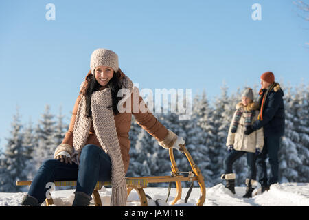 Junge Menschen genießen sonnige Winterschnee posiert auf Holzschlitten Stockfoto