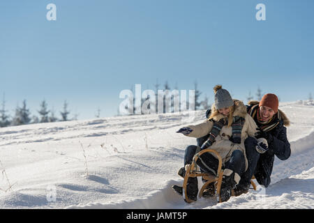 Junge verspielte Paare, die Spaß im Schnee Rodeln bergab Stockfoto