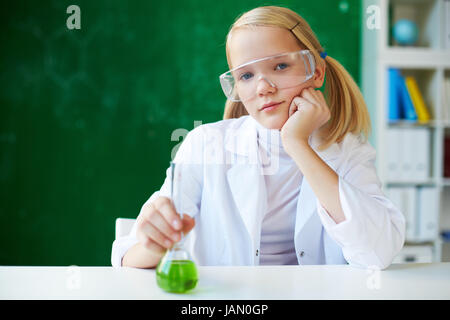 Porträt der niedliche Schulmädchen mit chemischen Flüssigkeit vorne am Arbeitsplatz sitzen Stockfoto