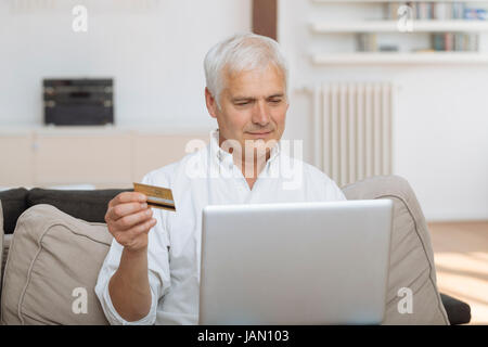 reifer Mann mit seinem Laptop und hält seine Kreditkarte Stockfoto