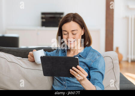 Reife Frau mit Tablet-PC, während Sie gemütlich auf dem Sofa zu Hause Stockfoto