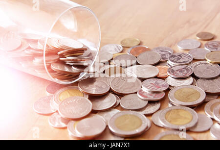 Konzept Geld zu sparen. Die Geld-Münze ist aus einer Glasflasche auf dem Holz Hintergrund verstreut. Stockfoto