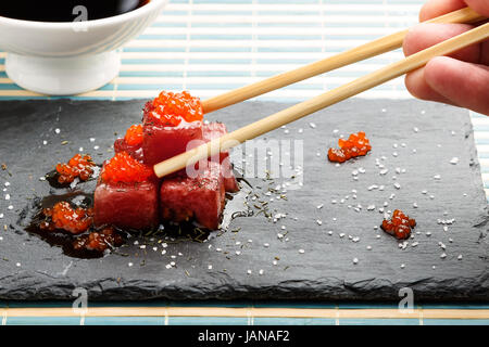 Thunfisch-Sashimi eingetaucht in Soja-Sauce mit Lachsrogen, dick Salz und Dill auf Schiefer mit Stäbchen und Schüssel mit Soja. Roher Fisch in traditionelle japanische Stockfoto