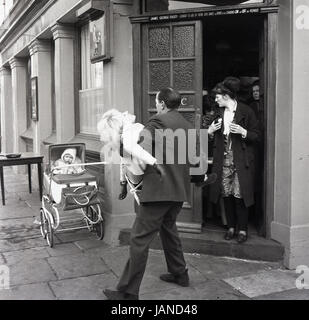 1965, historische, Bild zeigt einen Mann mit einer Dame vor dem Eingang zu einer Gastwirtschaft, die Erschöpfung nach den jährlichen Pfannkuchen Rennen Old Kent Road, Peckham, London zusammengebrochen. Beachten Sie, dass ein Baby in einem Kinderwagen eigenständig außerhalb der Kneipe gelassen hat. Stockfoto