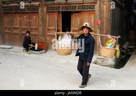 ZHAOXING, CHINA - 12. November 2010: Bewohner der Zhaoxing ist eine hübsche Dong Minderheit Stadt tragen von Gegenständen auf dem Stick für den Verkauf Stockfoto