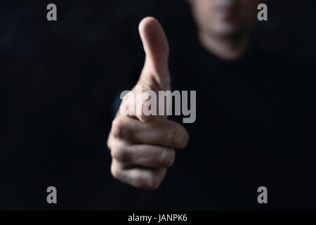 Closeup von einem kaukasischen Jüngling zeigt seinen Zeigefinger in den Vordergrund, die vorgeben, dass es eine Pistole vor einem schwarzen Hintergrund ist Stockfoto