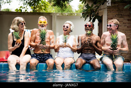 Gruppe von diverse ältere Erwachsene sitzen am Pool Ananas zusammenhalten Stockfoto