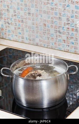 Simmering Hühnerbrühe mit würzen Gemüse im Stahltopf auf Glas Keramik Herd Stockfoto