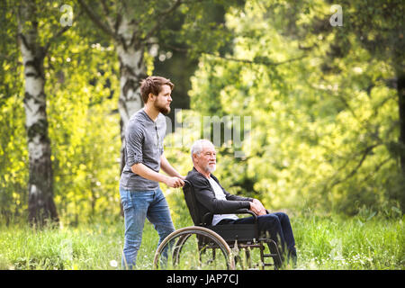 Hipster-Sohn mit behinderten Vater im Rollstuhl im Park spazieren. Stockfoto