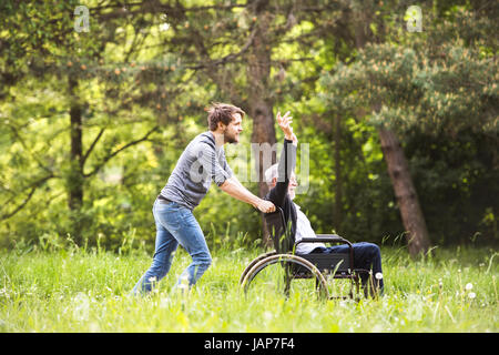 Hipster-Sohn mit behinderten Vater im Rollstuhl im Park spazieren. Stockfoto