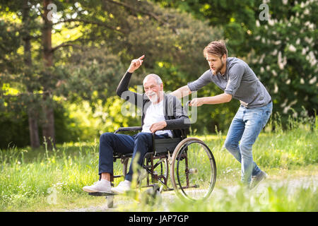 Hipster-Sohn mit behinderten Vater im Rollstuhl im Park spazieren. Stockfoto