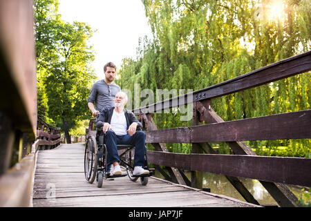 Hipster-Sohn mit behinderten Vater im Rollstuhl im Park spazieren. Stockfoto