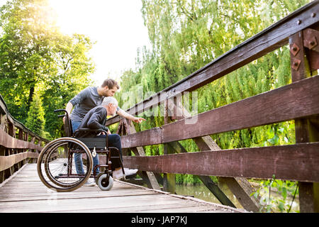 Hipster-Sohn mit behinderten Vater im Rollstuhl im Park spazieren. Stockfoto