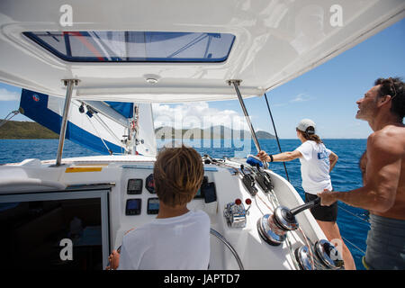 ein kleiner Junge am Ruder Segeln Katamaran in das türkisfarbene Wasser des karibischen Meeres aus den British Virgin islands Stockfoto