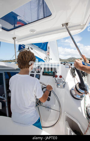 ein kleiner Junge am Ruder Segeln Katamaran in das türkisfarbene Wasser des karibischen Meeres aus den British Virgin islands Stockfoto