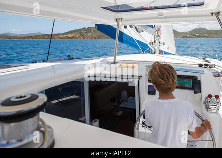 ein kleiner Junge am Ruder Segeln Katamaran in das türkisfarbene Wasser des karibischen Meeres aus den British Virgin islands Stockfoto