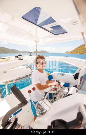 ein kleiner Junge am Ruder Segeln Katamaran in das türkisfarbene Wasser des karibischen Meeres aus den British Virgin islands Stockfoto