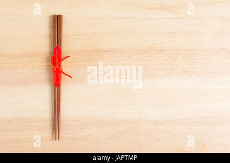 Japanische Essstäbchen aus Holz verpackt in rotem Papier und roten Seil auf Holztisch. Stockfoto