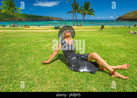 Frau zum Entspannen in der Hanauma Bay Nature Preserve, Oahu, Hawaii, USA. Lächelnde Frau in schwarzen Beachwear, Schlapphut, Sonnenbrille genießen auf tropische Urlaubsgebiete Stockfoto
