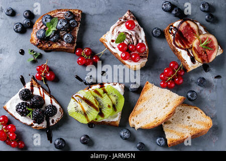 Große Auswahl an Dessert Sandwiches mit Beeren und Sahne Käse und Schokolade Wirbel. Rote Johannisbeeren, Blaubeeren, in Scheiben geschnittenen Kiwi, Feigen über grau Metall Zeitmessung Stockfoto