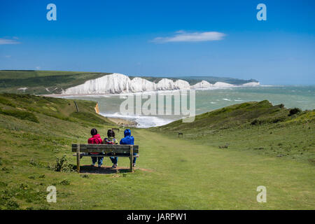 Menschen sitzen auf einem Sitz auf dem Vanguard Way in der Nähe von Cuckmere Haven, East Sussex, Großbritannien, mit den Kreidefelsen der Sieben Schwestern in der Ferne. Stockfoto