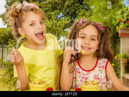 Zwei schöne junge Mädchen, eine gesundes Obst-Salat mit einer Gabel in einem Garten zu essen vorbereiten. Stockfoto