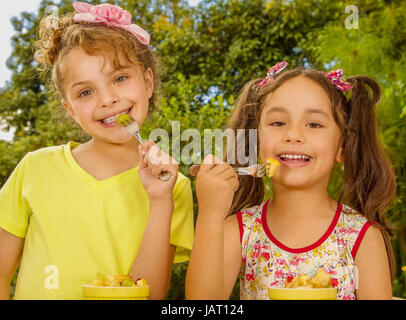 Zwei schöne junge Mädchen, eine gesundes Obst-Salat mit einer Gabel in einem Garten zu essen vorbereiten. Stockfoto