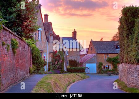 Cotswold Hütten mit Stockrosen und Rosen bei Sonnenuntergang, Mickleton in der Nähe von Chipping Campden, Gloucestershire, England. Stockfoto