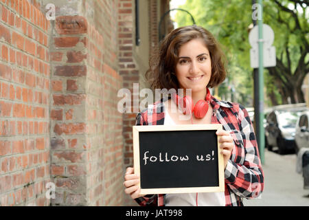 Junge schöne Frau mit Tafel mit Text "Folge uns". Social-Media-Konzept. Im Freien. Stockfoto