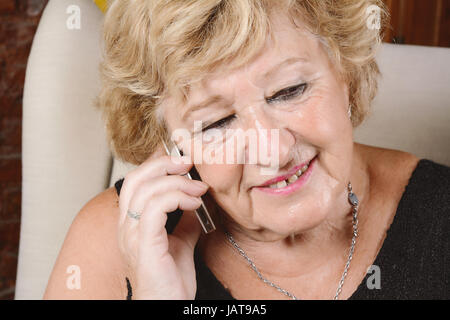 Porträt einer alten Frau am Telefon zu sprechen und auf Couch sitzen. Im Innenbereich. Stockfoto