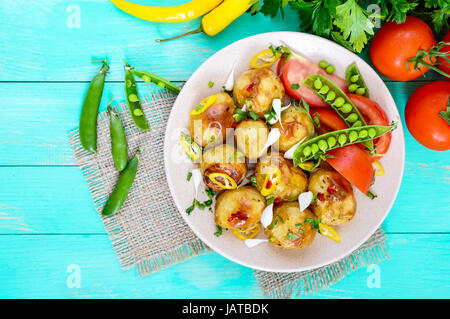 Würziger Salat aus gebackenen Kartoffeln, junger Knoblauch, Tomaten, grüne Erbsen auf einem Teller auf einem hellen Hintergrund. Ansicht von oben. Stockfoto