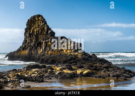 Eine große Felsformation am Strand glänzt mit Farbe von dem Licht reflektiert das Wasser unten. Stockfoto