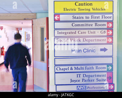 Signage in einem NHS-Krankenhaus in Großbritannien als Patient Spaziergänge durch den Rahmen, verschwommenes durch seine Bewegung im Krankenhaus Flur Stockfoto