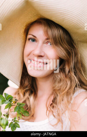 Frühling, Sommer, Urlaub, Natur, Schönheit, Dekoration, Gartenbau Konzept - close-up der schöne blauäugige Frau im Strohhut mit wallendem Haar und Fr Stockfoto