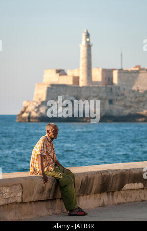 Havanna, Kuba - ca. Mai 2011: Älterer kubanischer Mann entspannt an der Wand des Malecon mit dem Morro Leuchtturm im Hintergrund. Stockfoto