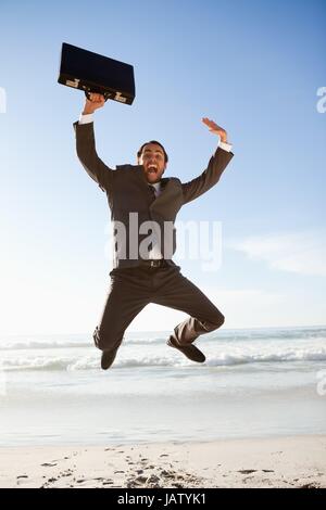 Junger Geschäftsmann springen am Strand Stockfoto