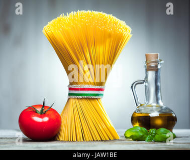 Bündel von rohem getrocknete italienische Spaghetti, verbunden mit einem Band in den Farben der Nationalflagge - rot, weiß und grün - mit einem Dekanter von Olivenöl, Basilikum und Tomaten Stockfoto