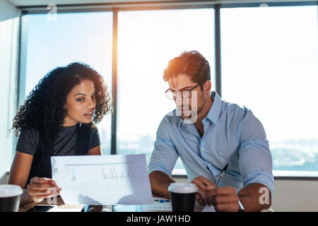 Junge Unternehmerin zeigt eine Papier zu ihrem Geschäftspartner beim Business-Pläne zu diskutieren. Junger Mann und Frau, sitzt am Tisch im Büro Analyse Stockfoto