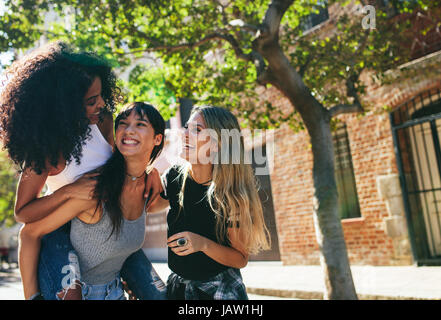 Gruppe von Freundinnen, die gemeinsam Spaß am Stadtstraße. Hispanic Frau mit afrikanischen auf Rücken mit kaukasischen Frau stand und lächelnd. Stockfoto